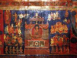 Tibet Guge 07 Tsaparang Red Temple 10 Band Life of Buddha  nowhere has it (the life of Buddha) been represented with so many details, with such a richness of scenes and with such a movement as here at Tsaparang. These frescoes have to be singled out as works of art.  Still above, the Buddha standing with the pindapatra in his right hand, indicates his resolution to deliver the famous first sermon. He starts walking towards Sarnath and en route meets the ajivaka Upagana, here represented with the ascetic stick: it is to him that he reveals his proposal to go to Banares to preach the law. The scene of preaching is, in fact, represented on the following panel. The Buddha sits on a throne covered by a rich canopy, with his hands in the attitude of the preaching mudra. On the basement of the throne are the traditional symbols of this culminating moment in the life of the Saint of the Sakyas namely, in the middle, the wheel representing, according to ancient symbolism, the first preaching; and on both sides two deer, reminding of the park actually called the Deer Park, where the famous ceremony was pronounced. Around him, in the act of devoted concentration and kneeling as a mark of homage, is a numerous crowd of every kind of creature: garuda above, nagas slightly below, gandharva and kinnaras, and then deities guided by Brahma and ascetics. The five emaciated yogins praying in the foreground possibly reproduce his first disciples. - Giuseppe Tucci: The Temples of Western Tibet and their Artistic Symbolism (1935). Photo - Weyer/Aschoff: Tsaparang, Tibets Grosses Geheimnis.